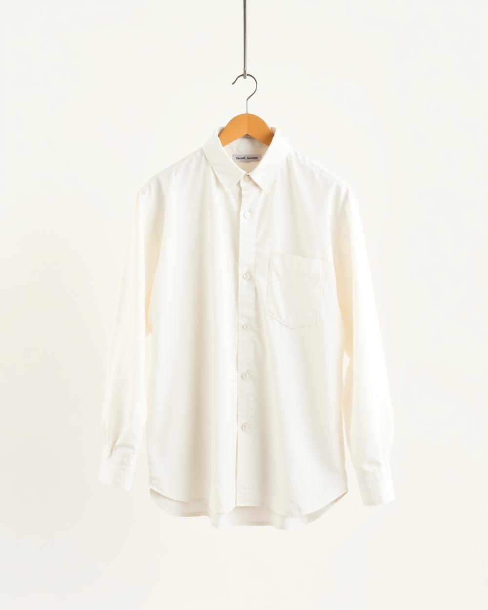 Chemise oversize blanche sur cintre devant un fond blanc cassé